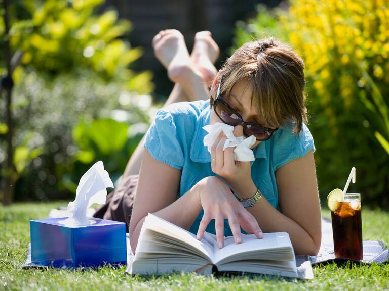 A woman suffering from hay fever while sunbathing in her garden.