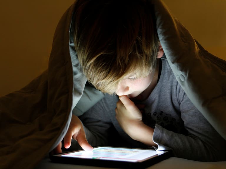 Boy using digital tablet under bed covers at night