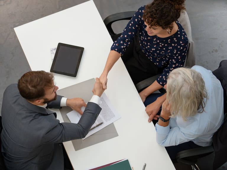 High angle view of adult couple shaking hands with lawyer after signing contract