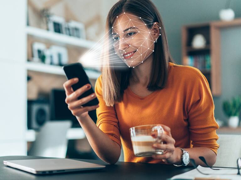 Facial recognition software scans the face of young woman holding smart phone at home