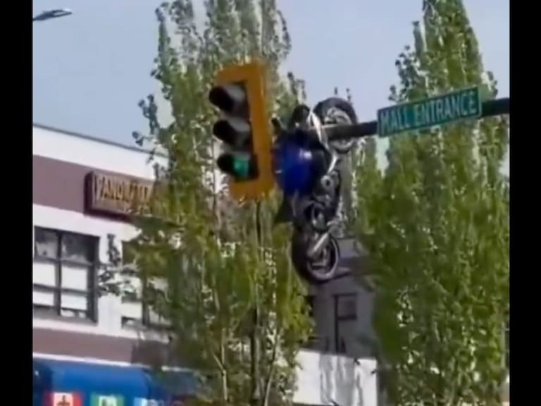 Se observa la motocicleta completamente suspendida sobre la estructura metálica del semáforo. X