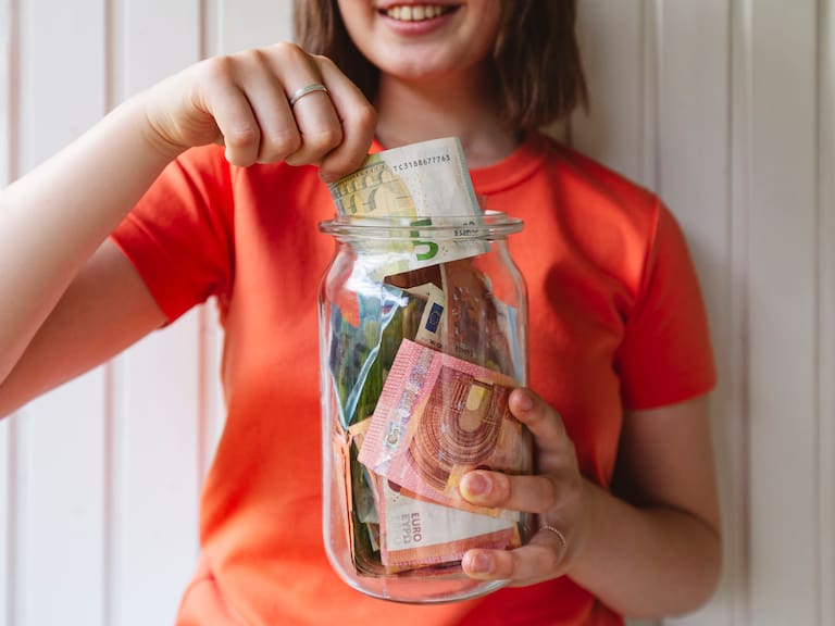 Girl removing five euro banknote from glass jar
