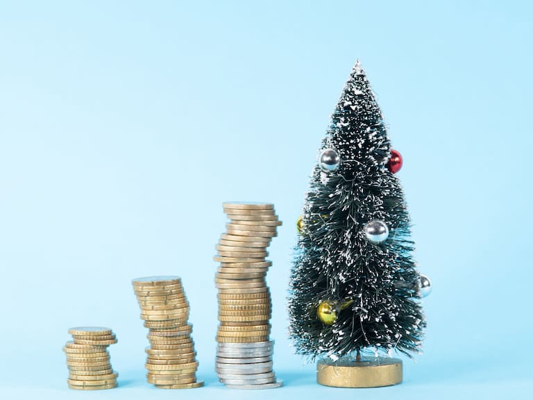 More money is needed to buy gifts and other things. Growing piles of coins close to a Christmas tree.