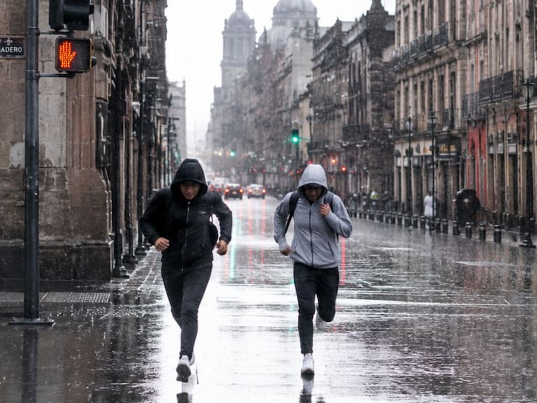 Dos personas corren por calles del Centro de la CDMX mientras cae una fuerte lluvia. IA