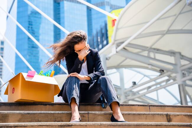 Persona frustrada, sentada en unas escaleras, al lado de una caja de cartón con sus pertenecias