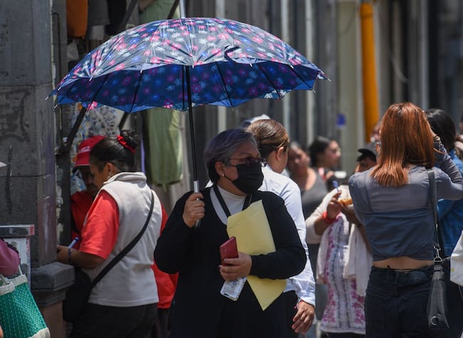 Persona mayor caminando por una calle de la ciudad de méxico con un paraguas para protegerse del sol