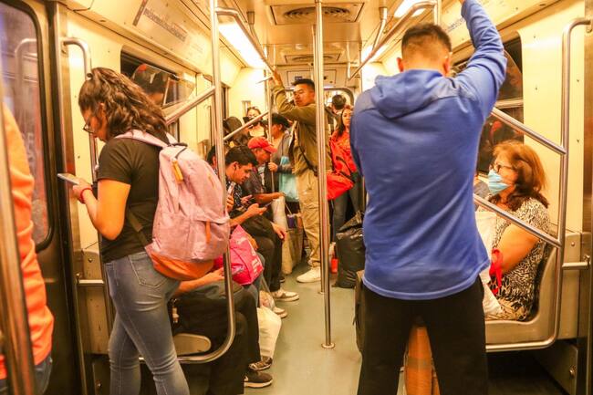 Personas sentadas y paradas viajando en el Metro de la Ciudad de México