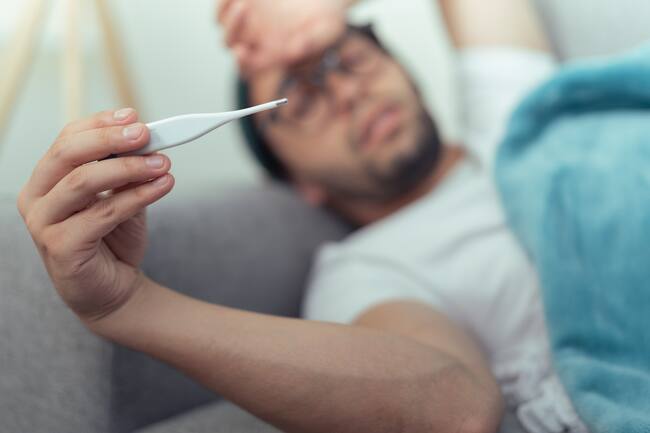 Persona recostada viendo el termómetro con expresiones de molestia